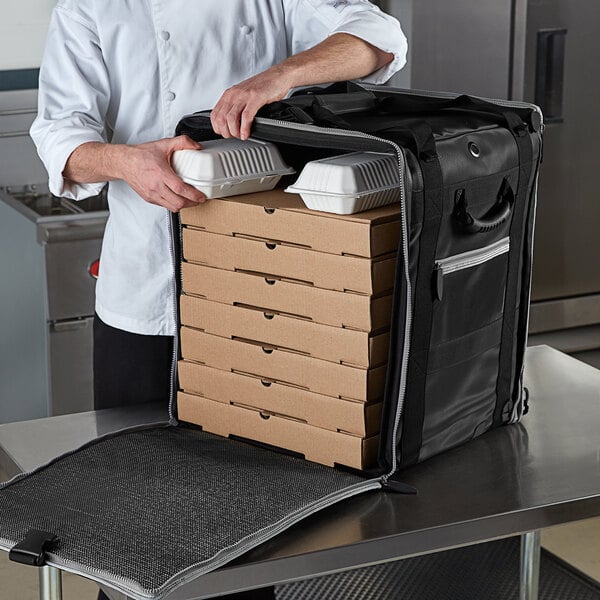 A chef using a Vollrath 5-Series insulated tower bag to hold pizza boxes.