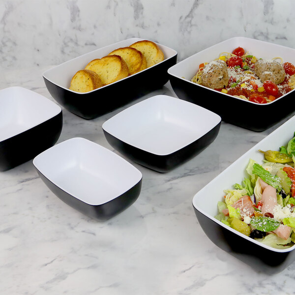 A group of black and white square bowls with food in them.