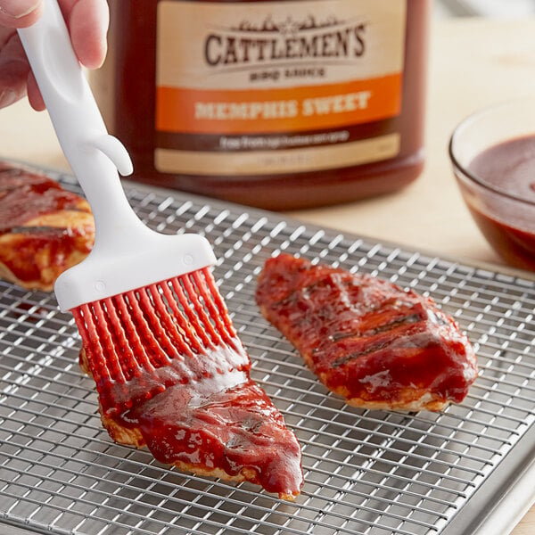 A person brushing Cattlemen's Memphis Sweet BBQ Sauce on meat on a metal rack.