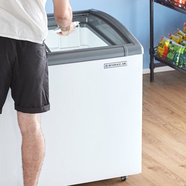 A man standing next to a Beverage-Air curved top display freezer in a room with white walls.
