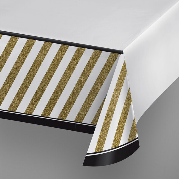 A white table with a Creative Converting black and gold striped tablecloth.