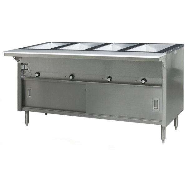 An Eagle Group stainless steel hot food table with sliding doors holding four pans on a counter in a large commercial kitchen.