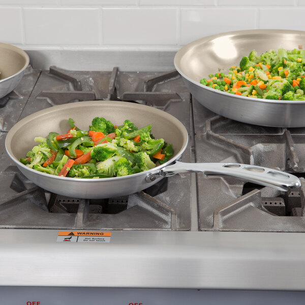 A Vollrath Wear-Ever aluminum non-stick fry pan with a bowl of vegetables on a stove.