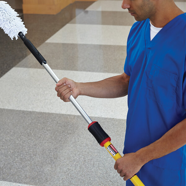 A man in blue scrubs using a Rubbermaid Quick-Connect telescopic pole to clean.