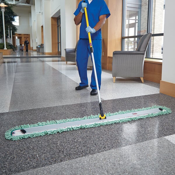 A man in a blue uniform using a Rubbermaid HYGEN microfiber mop on the floor.