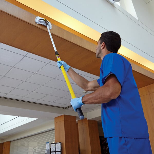 A man in blue scrubs using a Rubbermaid Quick-Connect telescopic pole to clean the ceiling.