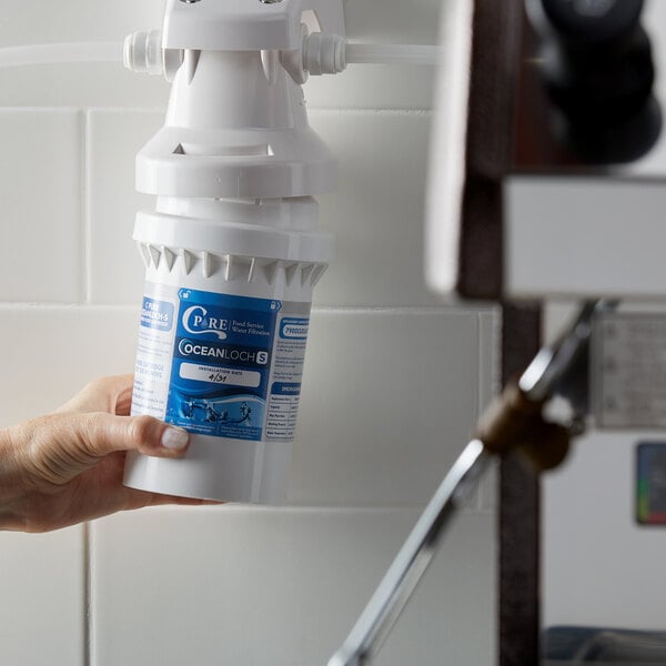 A hand holding a white C Pure water filter cartridge.