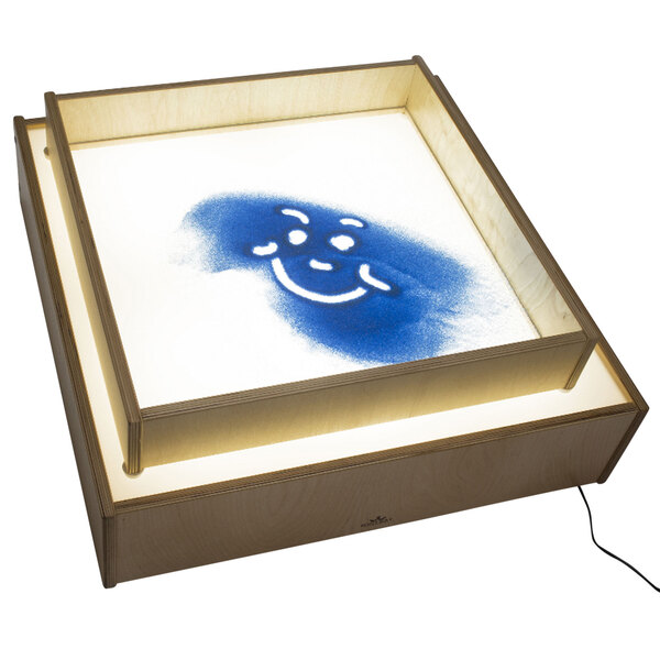A Whitney Brothers children's wood see-through sand box on a light table with a blue smiley face on it.