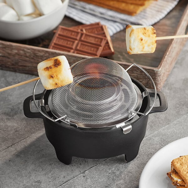 A Sterno S'mores Maker Jr. with a square marshmallow on a metal skewer over a small black pot.