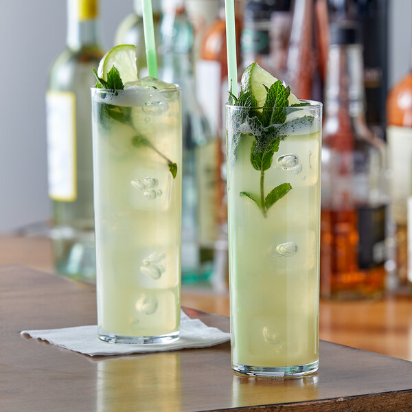 Two Arcoroc highball glasses filled with a lime and mint drink on a table.