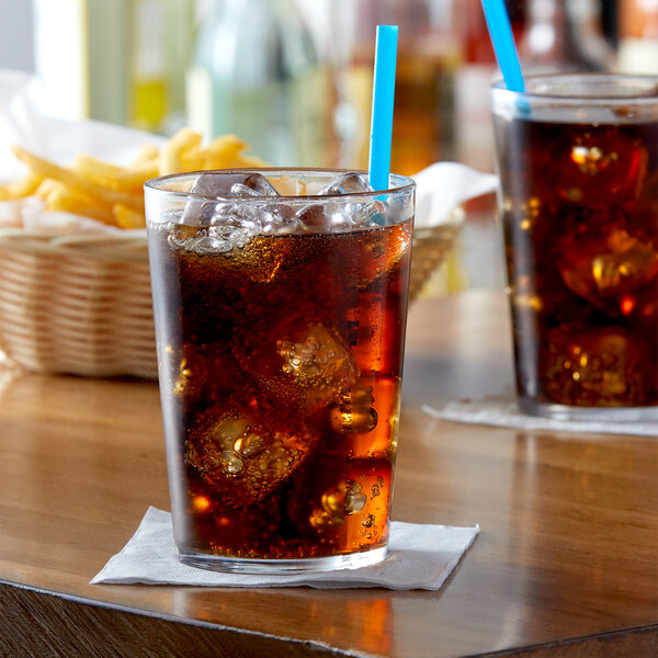 A glass of cola with ice cubes and a straw in an Arcoroc beverage glass on a table.