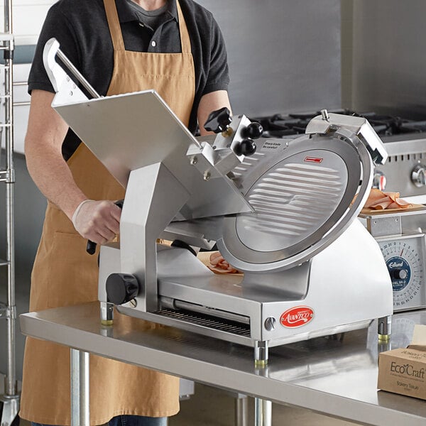 A man in an apron using an Avantco manual meat slicer on a kitchen counter.