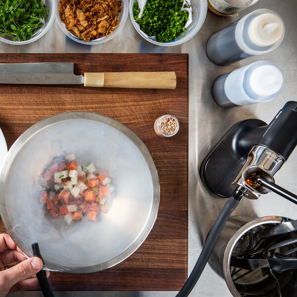 A person using a Breville Smoking Gun to smoke food in a bowl on a cutting board.