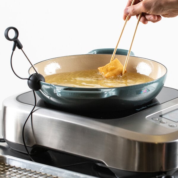 A person using chopsticks to stir food cooking on a Breville Control Freak induction range.