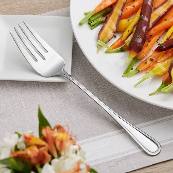 An Acopa Edgeworth stainless steel serving fork on a plate of food with carrots.
