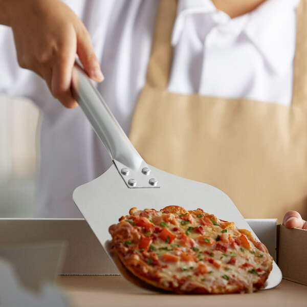 A person holding a Winco aluminum pizza peel with a pizza on it.