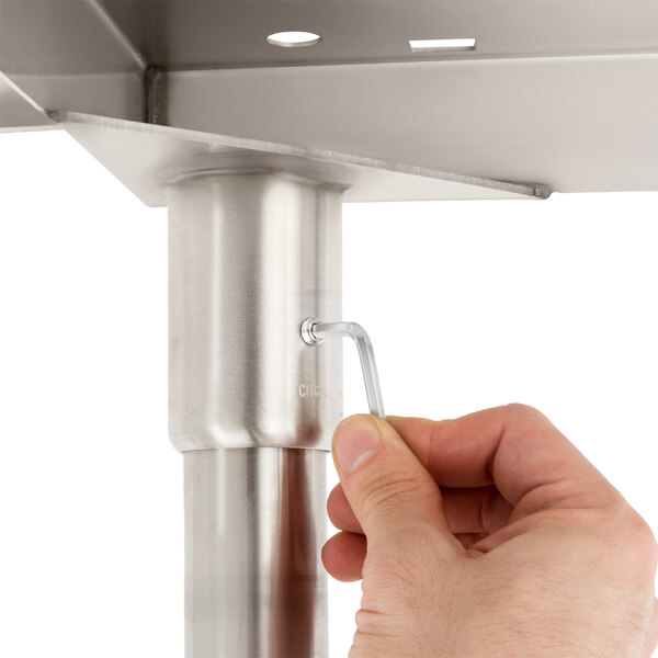 A hand using a screwdriver to attach a metal handle to a table.