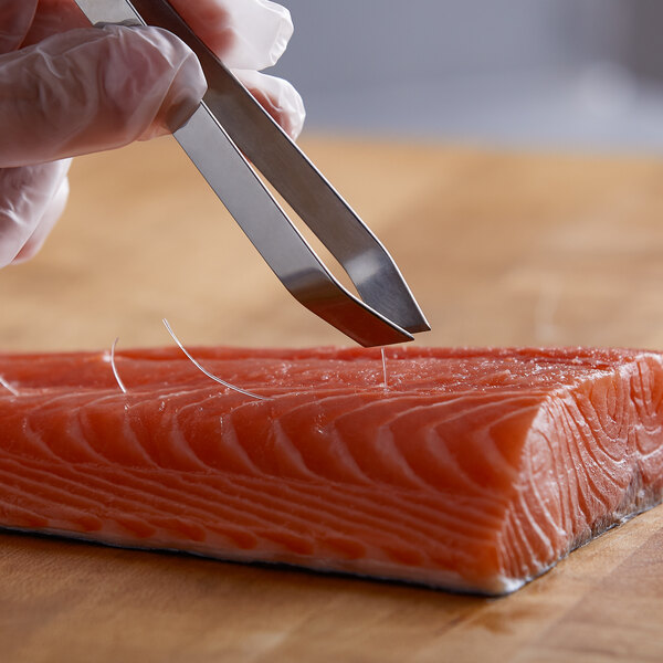 A person holding Dexter-Russell stainless steel culinary tweezers over a piece of fish.