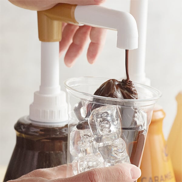 A hand pouring Torani dark chocolate sauce into a cup of ice.