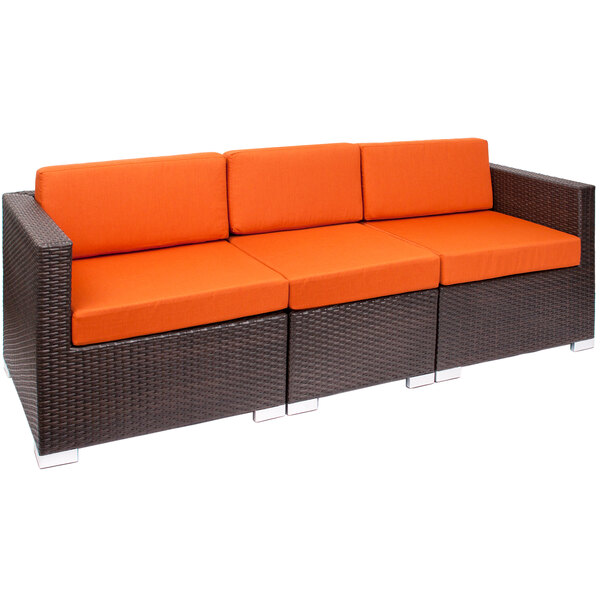 A BFM Seating Aruba Java wicker sectional sofa with orange cushions.