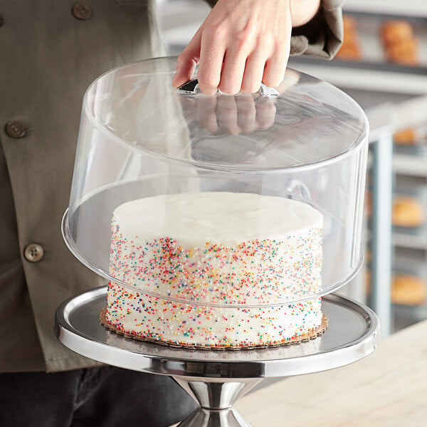 A hand holding a cake with a clear round cover.