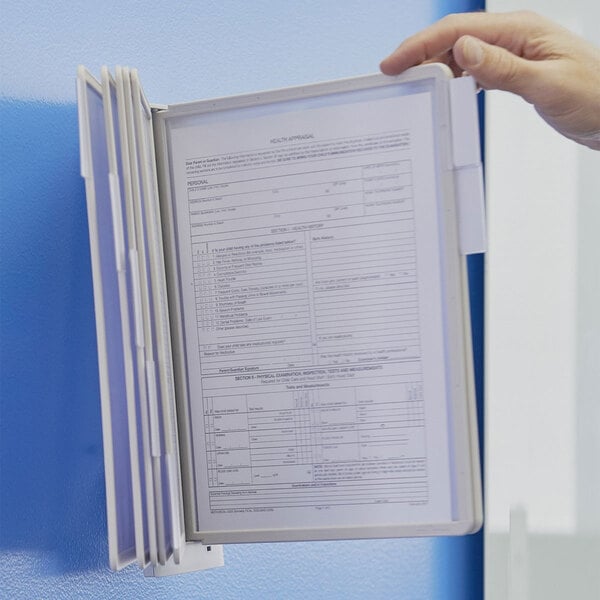A hand using a Durable Sherpa wall-mount reference system to view a document in a white folder.