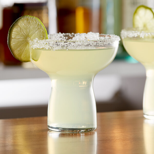 Two Libbey cocktail glasses with drinks and lime slices on a table.