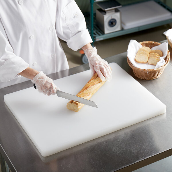 A person in white gloves using a knife to cut bread on a white polyethylene cutting board.