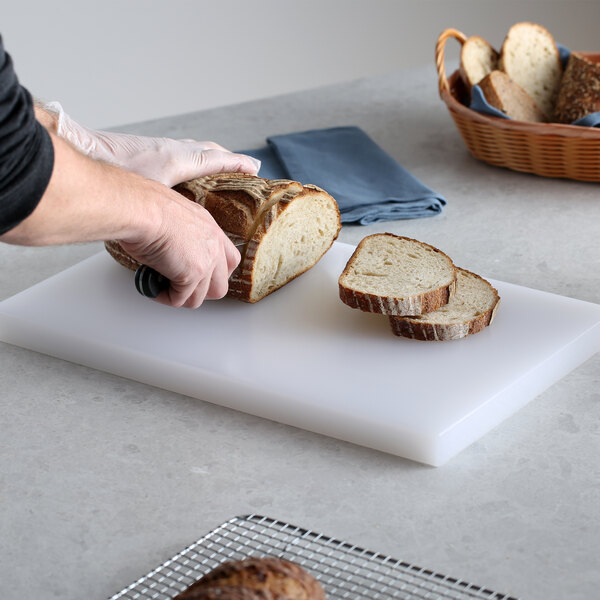 A person cutting a loaf of bread on a Thunder Group white polyethylene cutting board.