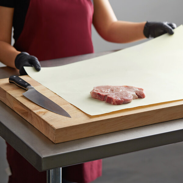 A person using a knife to cut meat on a Gardenia Premium paper-covered cutting board.