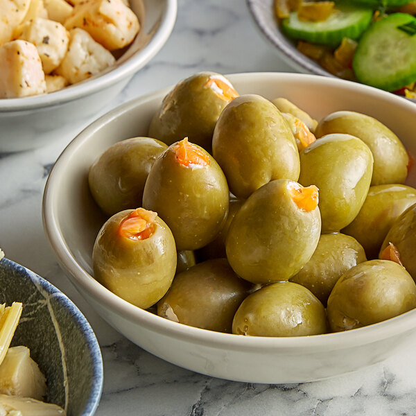 A bowl of green olives and food on a table.