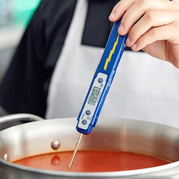 A person using a Comark waterproof digital pocket probe thermometer to check the temperature of soup.