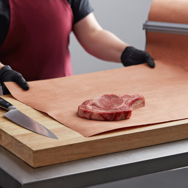 A person in a red apron using a knife to cut meat on a PeachTREAT Butcher Paper-covered cutting board.