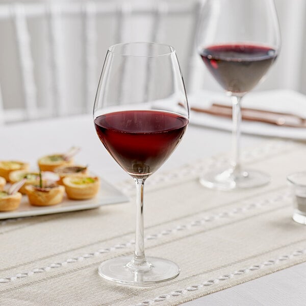 Two Acopa Bordeaux wine glasses filled with red wine on a table.