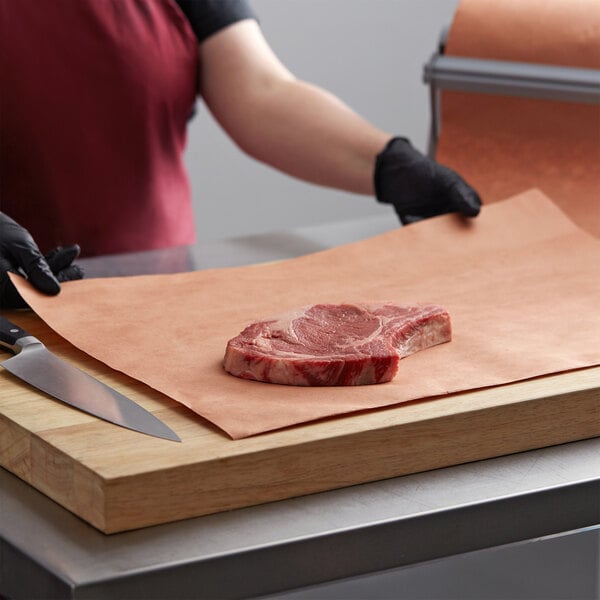 A person in a red apron using PeachTREAT Butcher Paper to hold a piece of meat on a cutting board.