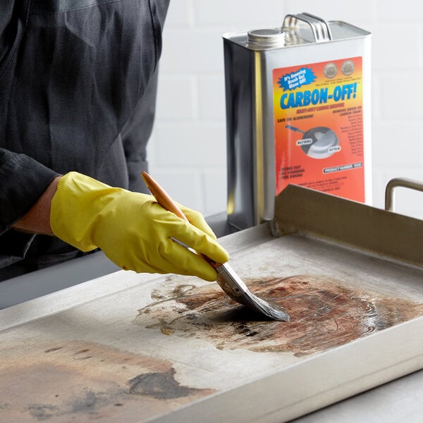 A person wearing yellow gloves using a brush to clean a dirty tray.
