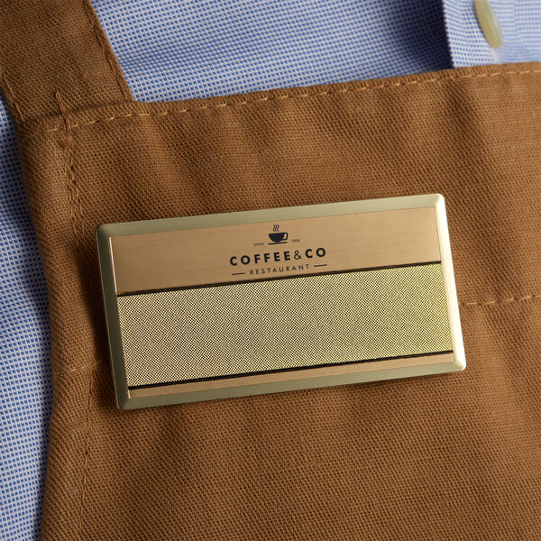 A close up of a gold rectangular Cawley nametag on a brown apron.