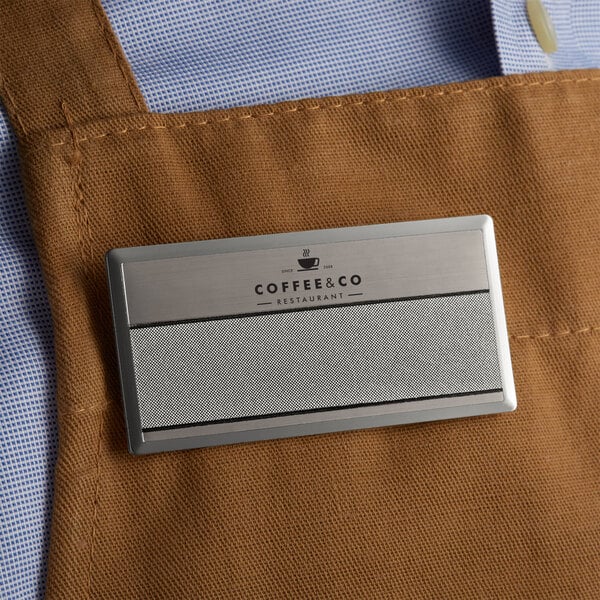 A close up of a customizable silver metal rectangle name tag with a logo.