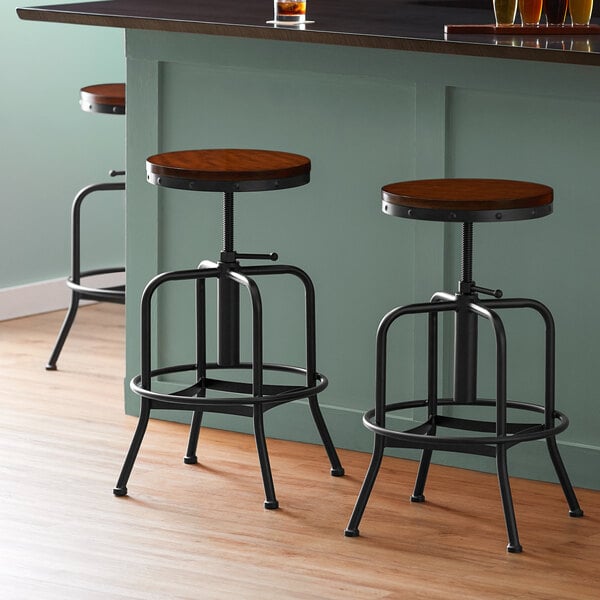 Three Lancaster Table & Seating black barstools with antique walnut seats at a counter.