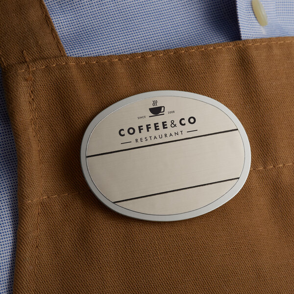 A coffee shop employee wearing a brown apron with a customizable white oval nametag.
