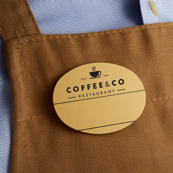 A brown apron with a customizable gold plastic oval nametag with a logo on it.
