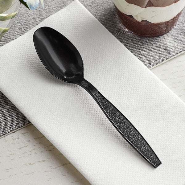 A Visions black heavy weight plastic teaspoon on a napkin.