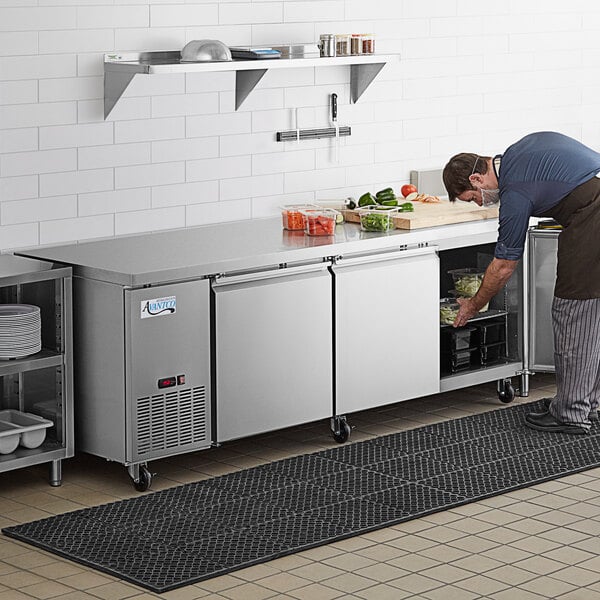 A man putting food into an Avantco undercounter refrigerator.