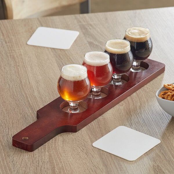 An Acopa mahogany finish flight paddle holding Belgian beer glasses filled with beer on a table.