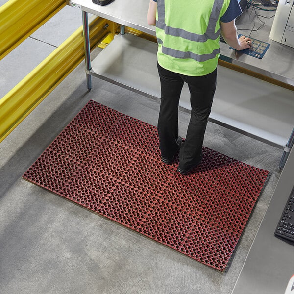 A person standing on a red Lavex heavy-duty anti-fatigue floor mat.