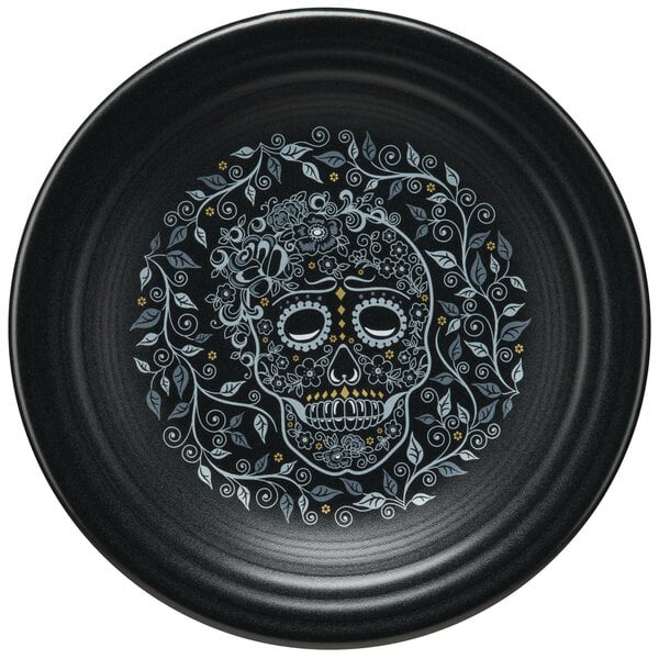 A black Fiesta luncheon plate with a skull, flowers, and leaves design.