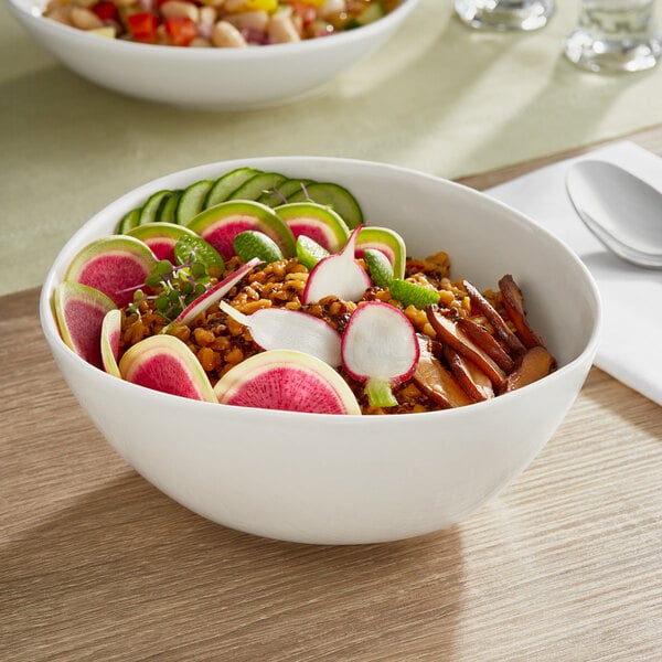 A close up of a bowl of food with vegetables and radishes in an Acopa Nova cream white stoneware bowl.