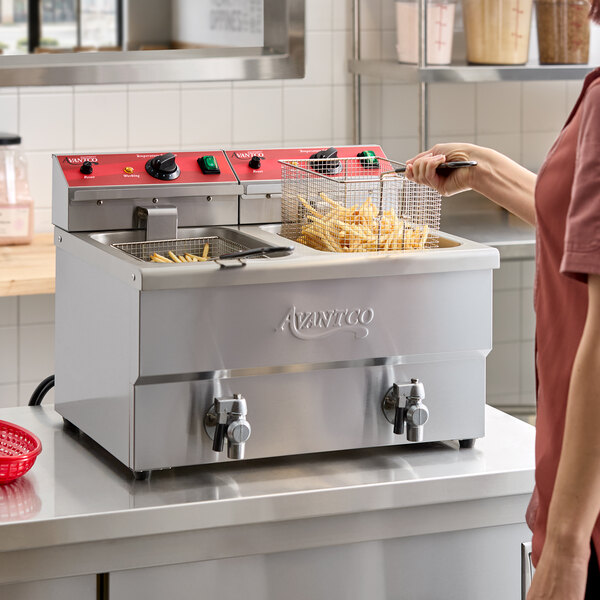A person is using a stainless steel dual tank electric countertop fryer to cook French fries in a commercial kitchen setting.