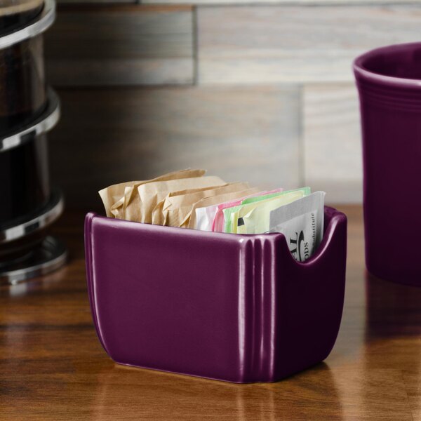 A purple ceramic Fiesta sugar caddy on a counter with sugar packets inside.