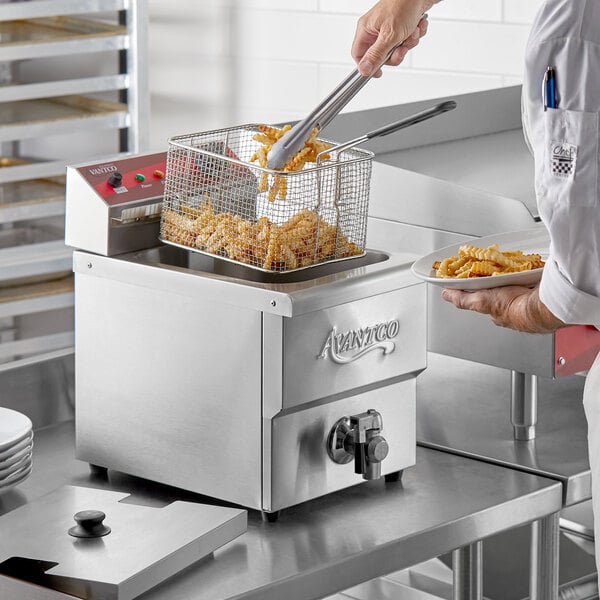A man using tongs to fry french fries in an Avantco electric countertop fryer.